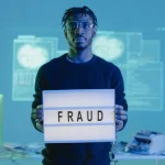 Computer hacker holding 'fraud' sign